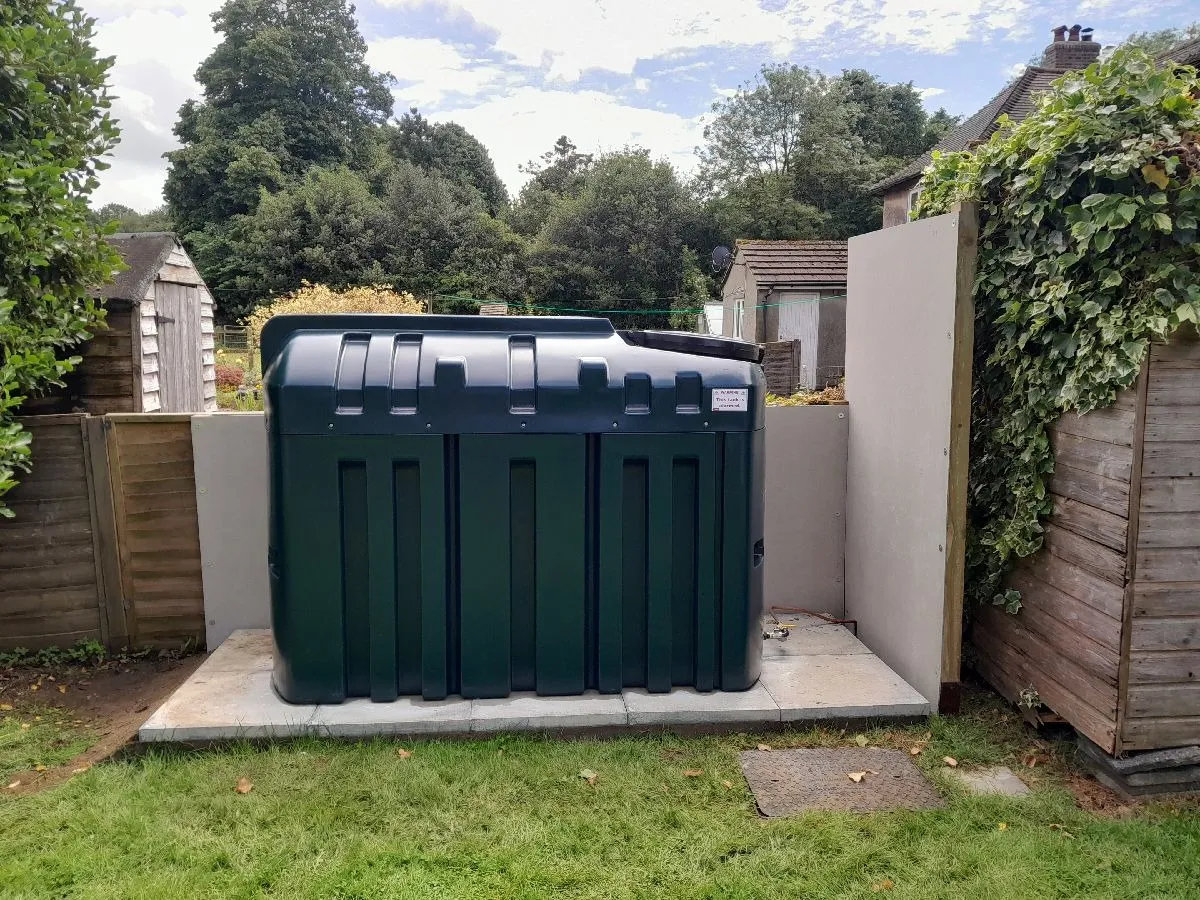 A large green trash can sitting in the middle of a yard.
